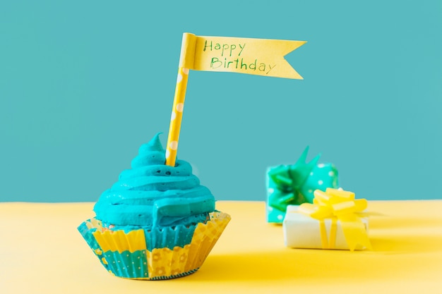 Photo délicieux muffin avec drapeau joyeux anniversaire près d'un cadeau sur une surface jaune