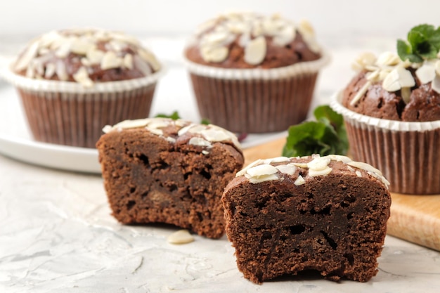 De délicieux muffins au chocolat sucrés, avec des pétales d'amande à côté de la menthe et des noix d'amande sur une table en béton léger. fermer