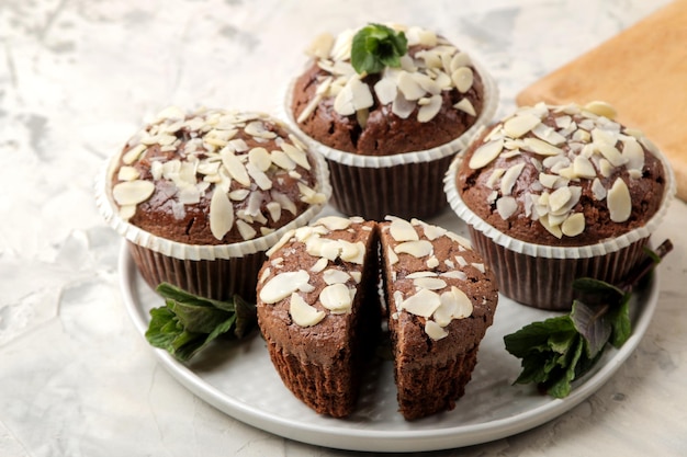 De délicieux muffins au chocolat sucrés, avec des pétales d'amande à côté de la menthe et des noix d'amande sur une table en béton léger. fermer