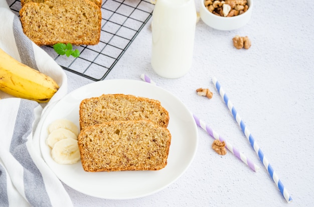 Délicieux pain aux bananes fait maison avec des noix et de la cannelle sur une plaque blanche avec une bouteille de lait et des bananes fraîches. Orientation horizontale. Fermer.