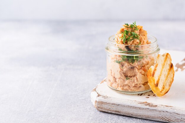 Délicieux pâté de poulet maison aux épices et à l'aneth dans un bocal en verre et une tranche de pain à proximité et câpres sur une table légère. Mise au point sélective.