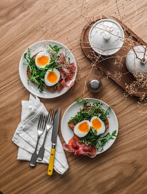 Délicieux petit déjeuner brunch sandwich grillé à grains entiers avec œuf dur à la roquette et prosciutto sur une table en bois vue sur le dessus