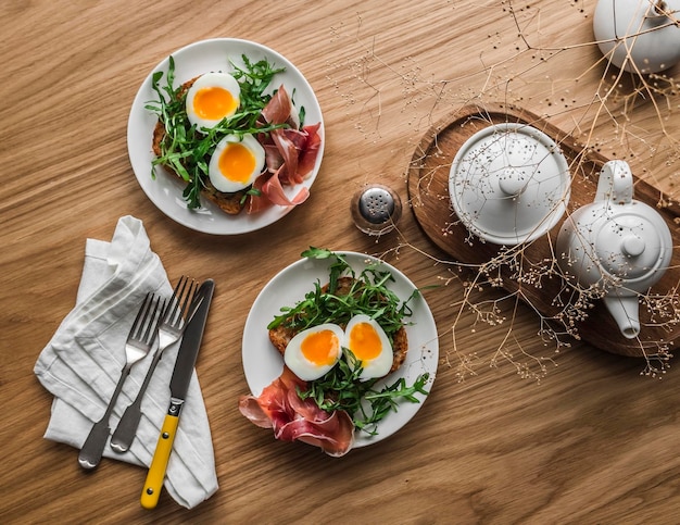 Délicieux petit déjeuner brunch toasté avec des œufs bouillis à la roquette et du prosciutto sur une table en bois