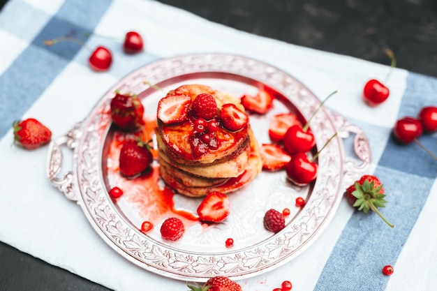 Délicieux petit déjeuner désert. Pile de crêpes aux fruits et confiture de fraises, framboises et cerises dans une plaque en laiton sur une table en bois rustique.