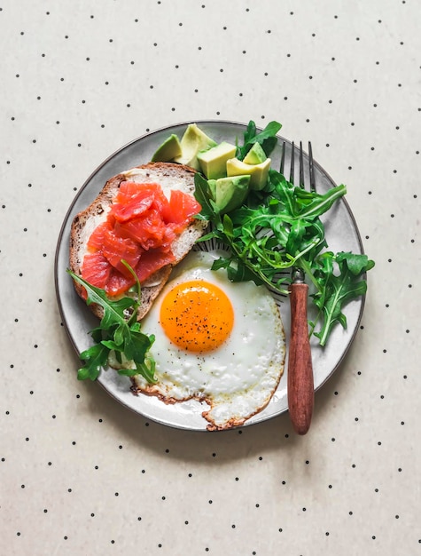 Délicieux petit-déjeuner équilibré œuf frit sandwich au saumon avocat et roquette sur fond clair vue de dessus