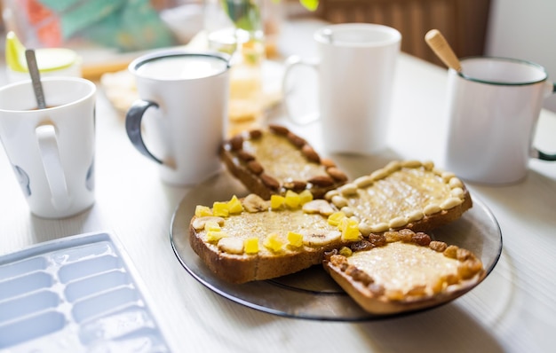 Un délicieux petit-déjeuner nutritif avec du thé et du café, du melon et de la banane coupés en morceaux, des toasts frais avec du beurre et des noix sont sur la table en attendant la compagnie ou la famille dans une cuisine familiale confortable le matin