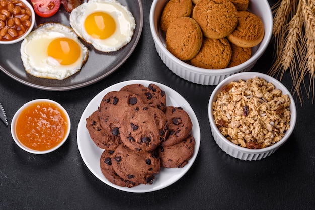 Un délicieux petit-déjeuner sain et nutritif avec des œufs au plat des haricots au bacon un verre de jus de biscuits à l'avoine du lait et de la confiture Une alimentation saine au début de la journée