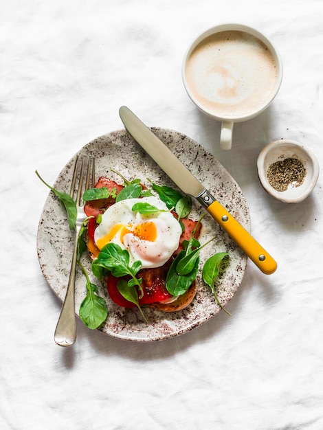 Délicieux petit-déjeuner sandwich avec jambon tomate oeuf poché roquette et café sur fond clair vue de dessus