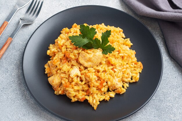 Délicieux pilaf asiatique, riz cuit aux légumes et poulet sur une assiette. fond de béton gris.