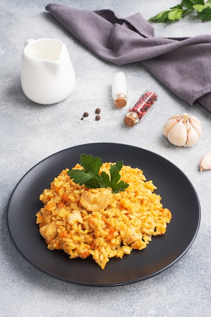 Délicieux pilaf asiatique, riz mijoté avec légumes et poulet sur une assiette. fond de béton gris.