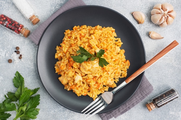 Délicieux pilaf asiatique, riz mijoté avec légumes et poulet sur une assiette. fond de béton gris.