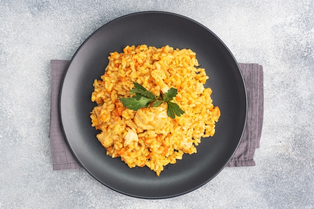 Délicieux pilaf asiatique, riz mijoté avec légumes et poulet sur une assiette. fond de béton gris.