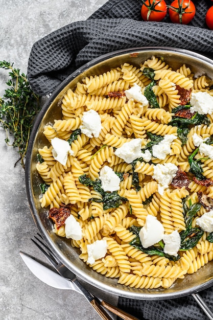 Délicieux plat de pâtes fusilli avec sauce crémeuse aux épinards et tomates séchées. Fond gris. Vue de dessus.