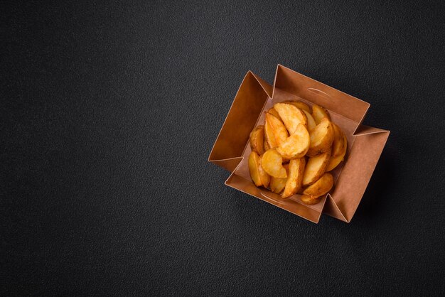 De délicieux quartiers de pommes de terre frites croustillantes avec des épices et des herbes salées sur un fond de béton foncé