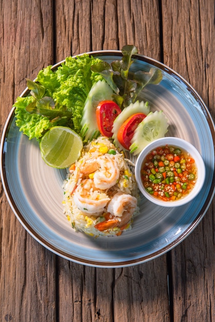 Délicieux riz frit aux crevettes, servi avec du piment frais et une salade de tomates au concombre, disposé sur un beau plat, posé sur une table en bois.