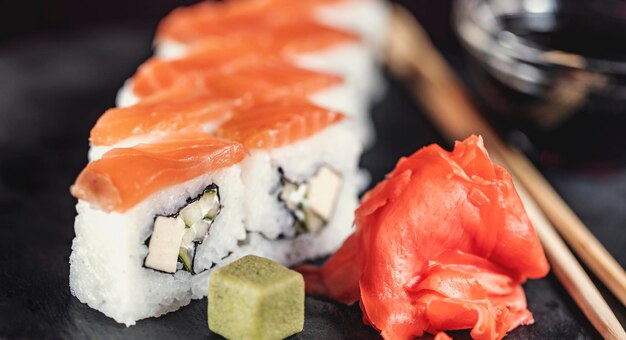 De délicieux rouleaux de riz à sushi sur une plaque en pierre noire avec de la sauce soja et des baguettes