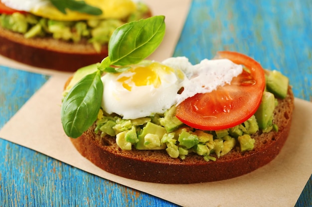 Délicieux sandwich à l'oeuf avocat et légumes sur une serviette en papier sur fond de bois de couleur