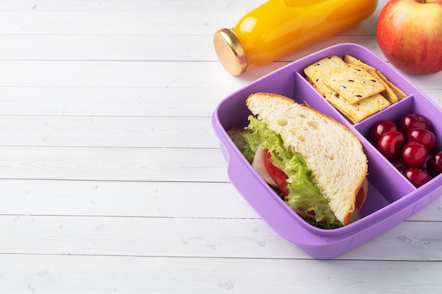 Délicieux sandwich sain dans une boîte à lunch, biscuits et cerises. Emportez le déjeuner avec vous à l'école ou au bureau. Jus dans une bouteille et une pomme.