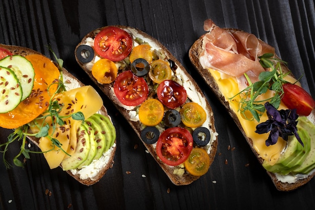 Délicieux sandwichs ouverts avec fromage à l'avocat, bacon, tomate cerise et olive