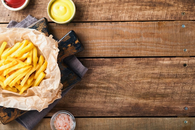 Délicieux serveur de frites sur papier parchemin sur une planche à découper en bois avec sauce tomate et fromage sur fond de table en bois Divers plats Keto Restauration rapide et concept d'aliments malsains