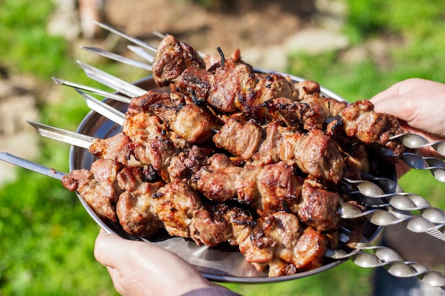 Délicieux shish kebab fraîchement cuit et juteux sur des brochettes sur un plateau tenu par un homme Pique-nique en plein air