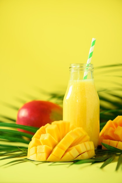 Délicieux smoothie juteux avec des fruits orange et de la mangue sur fond jaune Copie espace Pop art design concept d'été créatif Jus frais dans des bouteilles en verre sur des feuilles de palmier vert Bannière