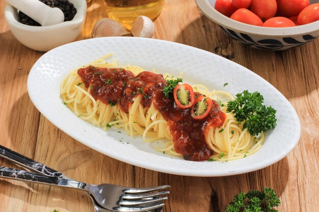 De délicieux spaghettis servis sur une assiette ovale blanche. Sur la table en bois