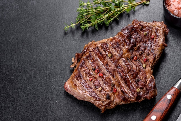 Délicieux steak de boeuf frais juteux avec des épices et des herbes sur un fond de béton foncé. Plats grillés