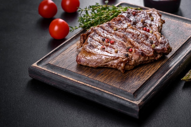 Délicieux steak de boeuf frais juteux avec des épices et des herbes sur un fond de béton foncé. Plats grillés