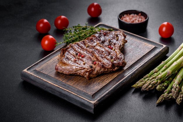 Délicieux steak de boeuf frais juteux avec des épices et des herbes sur un fond de béton foncé. Plats grillés