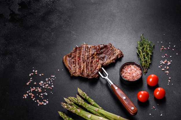 Délicieux steak de boeuf frais juteux avec des épices et des herbes sur un fond de béton foncé. Plats grillés