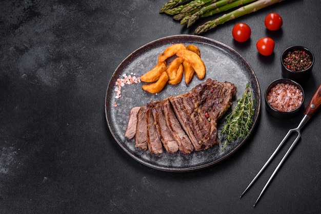 Délicieux steak de boeuf frais juteux avec des épices et des herbes sur un fond de béton foncé. Plats grillés