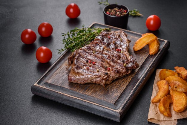 Délicieux steak de boeuf frais juteux avec des épices et des herbes sur un fond de béton foncé. Plats grillés