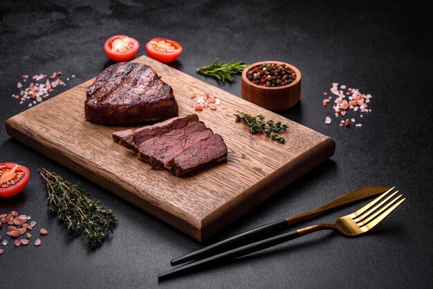 Délicieux steak de boeuf juteux frais avec des épices et des herbes sur un fond de béton foncé