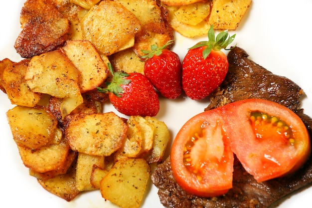 Photo un délicieux steak de boeuf avec des pommes de terre tranchées, des fraises et des tomates