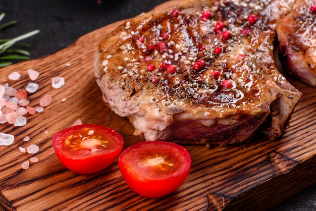 Délicieux steak juteux frais sur les os avec des légumes et des épices. Steak de porc juteux grill sur table sombre