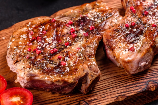 Délicieux steak juteux frais sur les os avec des légumes et des épices. Steak de porc juteux grill sur table sombre