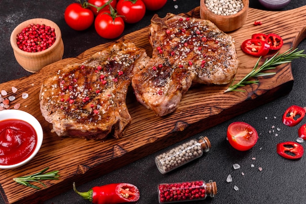 Délicieux steak juteux frais sur les os avec des légumes et des épices. Steak de porc juteux grill sur table sombre