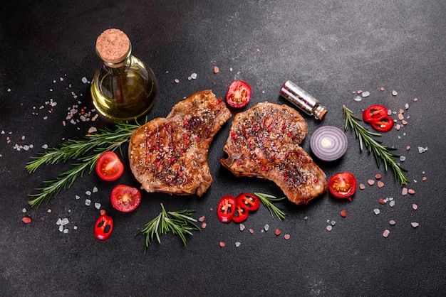 Délicieux steak juteux frais sur les os avec des légumes et des épices. Steak de porc juteux grill sur table sombre