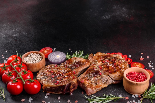 Délicieux steak juteux frais sur les os avec des légumes et des épices. Steak de porc juteux grill sur table sombre