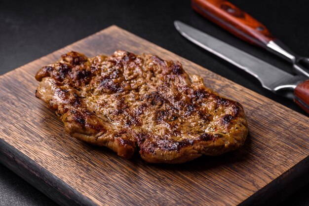 Délicieux steak de porc grillé juteux avec des épices et des herbes sur une planche à découper en bois