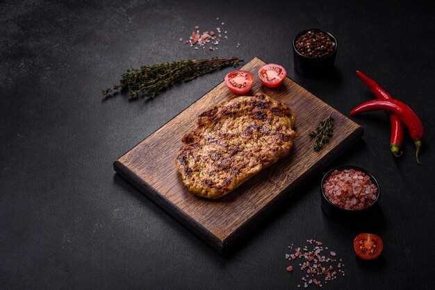 Délicieux steak de porc grillé juteux avec des épices et des herbes sur une planche à découper en bois