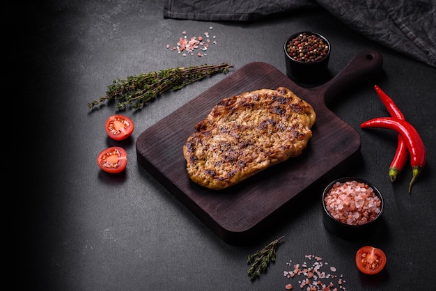 Délicieux steak de porc grillé juteux avec des épices et des herbes sur une planche à découper en bois