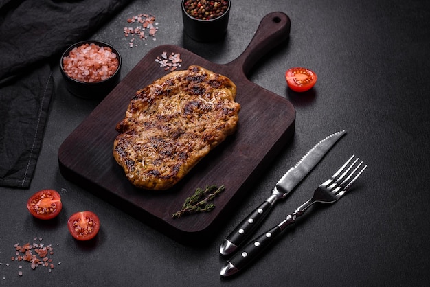 Délicieux steak de porc grillé juteux avec des épices et des herbes sur une planche à découper en bois