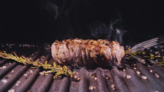 Délicieux steak de viande juteux cuit sur le gril Alevins de bœuf de choix sur rôtissoire électrique romarin poivre noir sel Ralenti