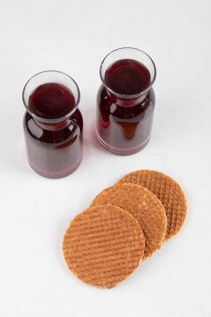 Délicieux stroopwafels avec garnitures au caramel et verre de jus de fruits frais sur une surface blanche