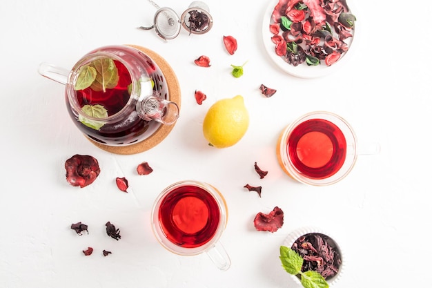 Délicieux thé aromatique d'hibiscus aux pétales de rose dans une théière avec des feuilles de menthe et du thé de guérison au citron pour la grippe et le rhume vue de dessus style plat