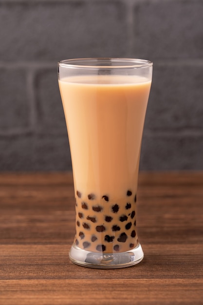 Délicieux thé au lait à bulles avec boule de perles de tapioca en verre sur table en bois