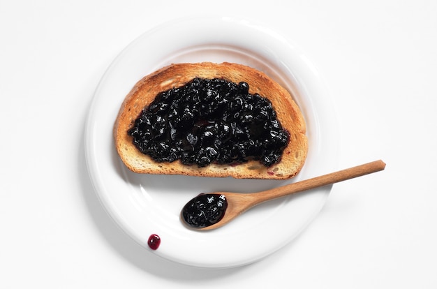 Délicieux toasts avec confiture de myrtilles dans une assiette sur fond blanc, vue de dessus