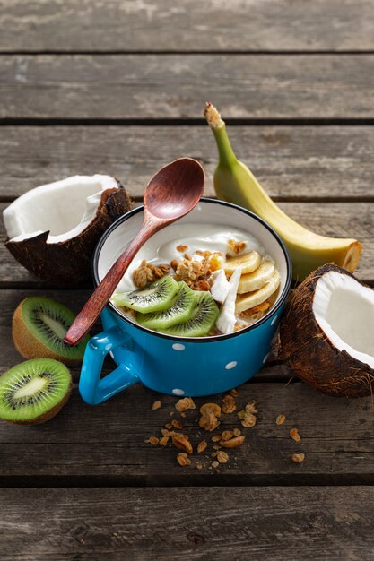 Délicieux yogourt à la noix de coco avec granola et fruits servi sur une table en bois rustique. Nourriture végétalienne saine. Concept de petit-déjeuner savoureux et sain